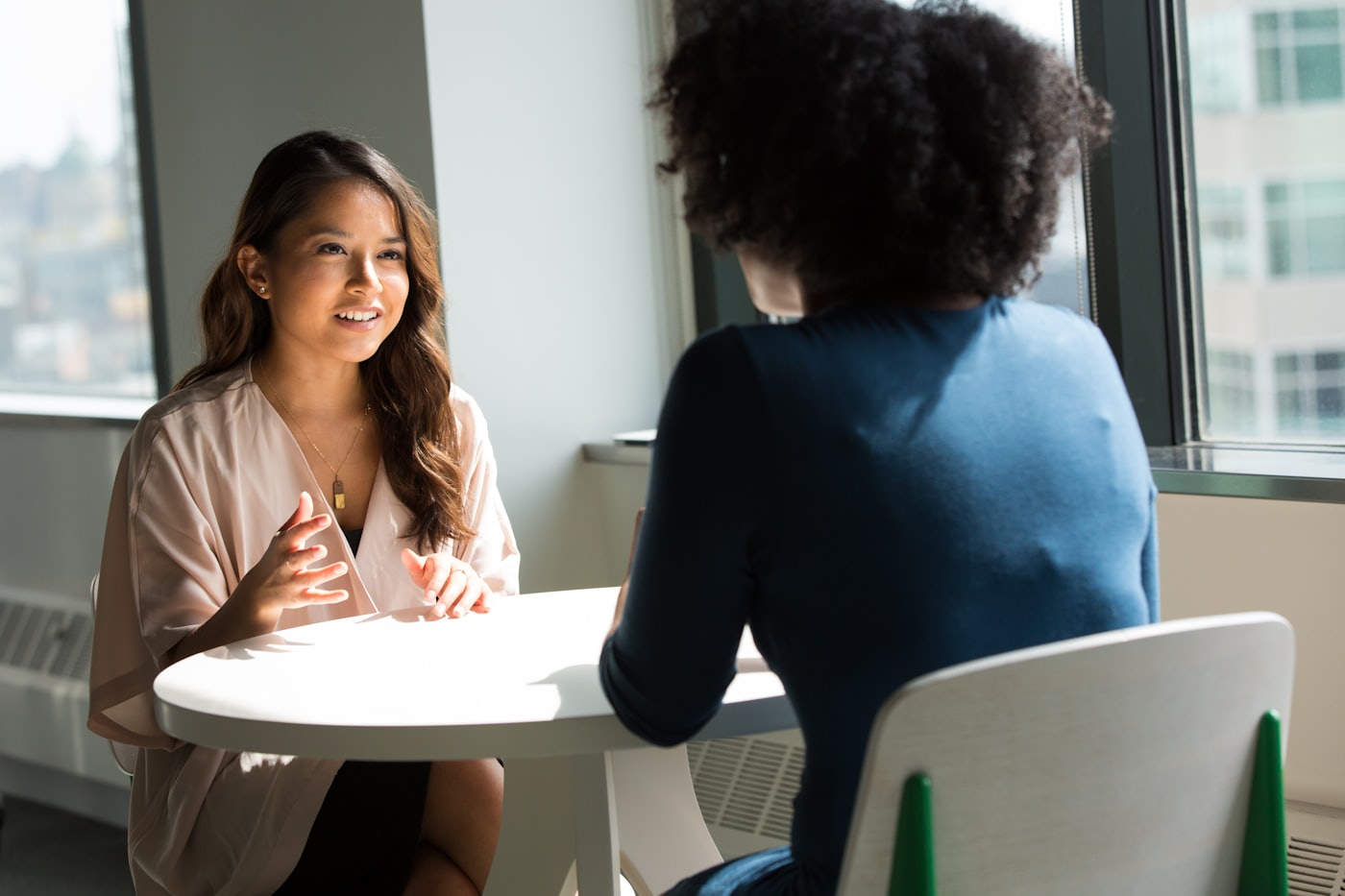 A calm one-on-one advisory conversation across a table by a window — real estate consultation