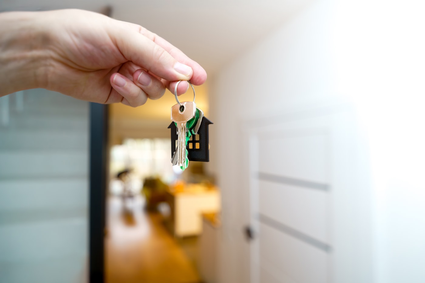 A hand holding house keys with a home interior softly blurred behind — new-home handover